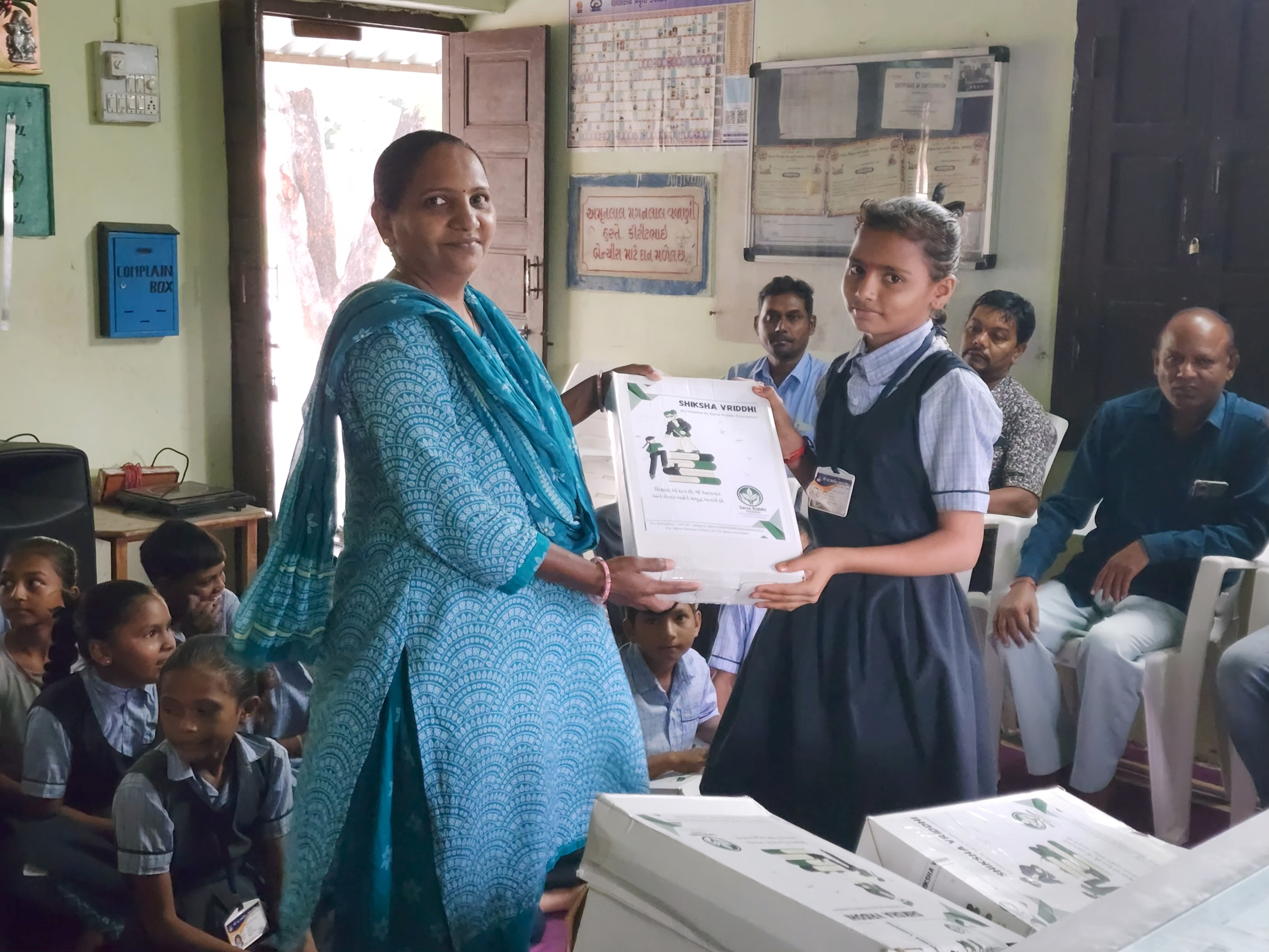 Girl receiving educational kit from a woman in blue indoors